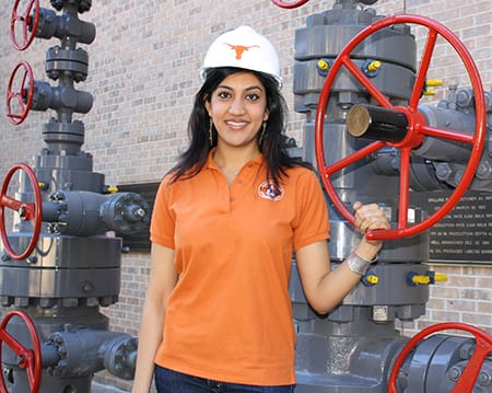 Sharma poses by pressure valves in a hardhat emblazoned with UT logo.