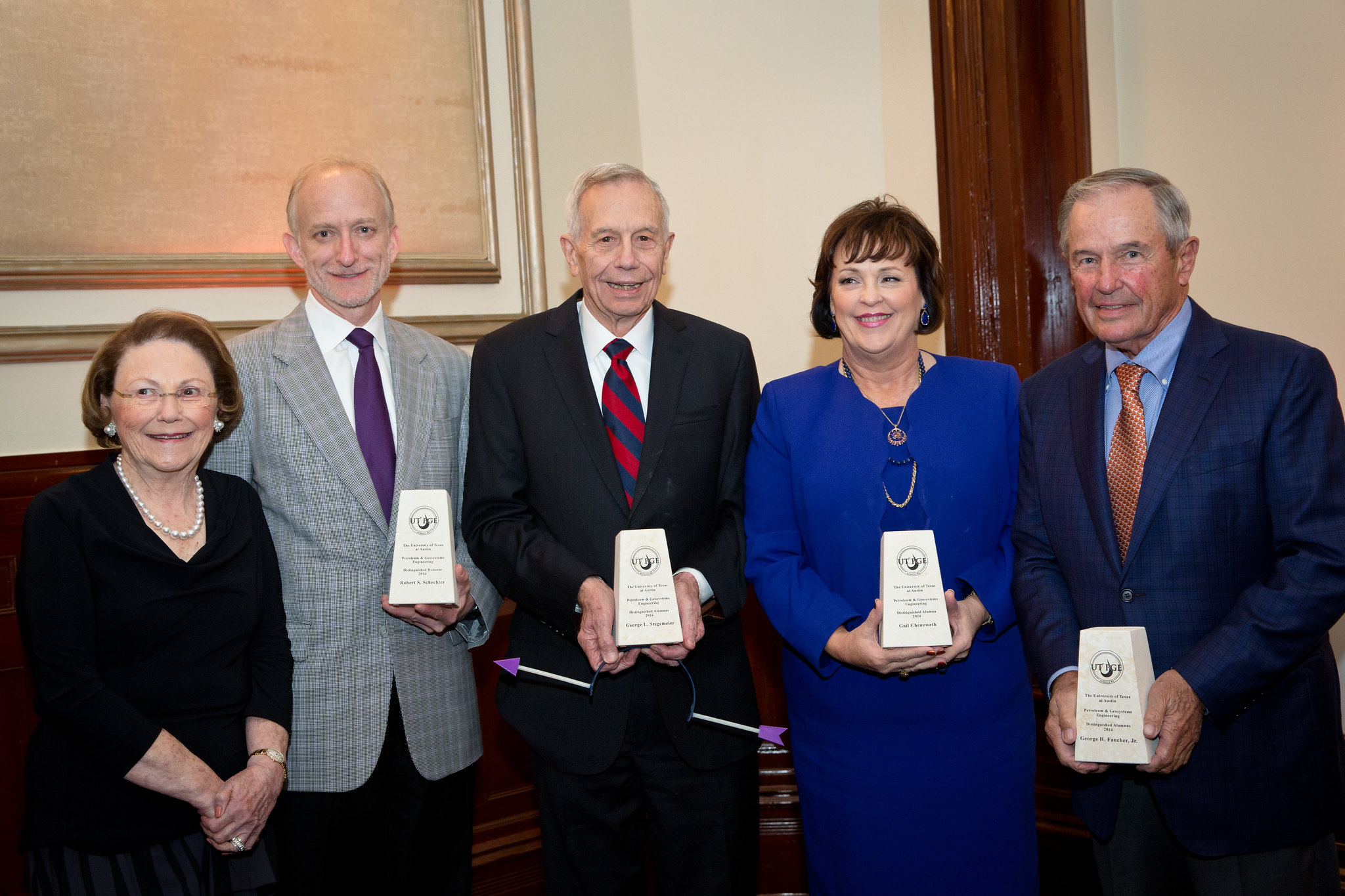 Distinguished alumni award recipients holding their awards and smiling.