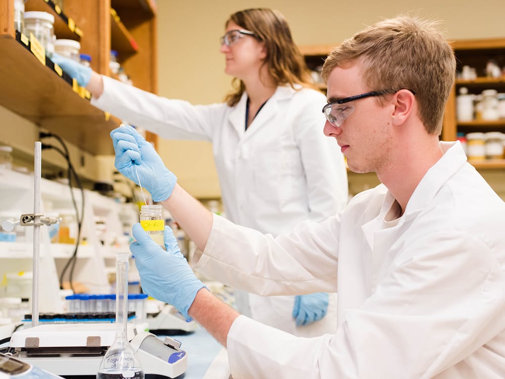 two people wearing lab coats and working in a lab environment