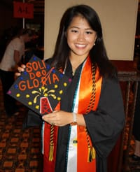 Renyut poses in graduation robes holding a mortarboard reading 'SOLI DEO GLORIA.'