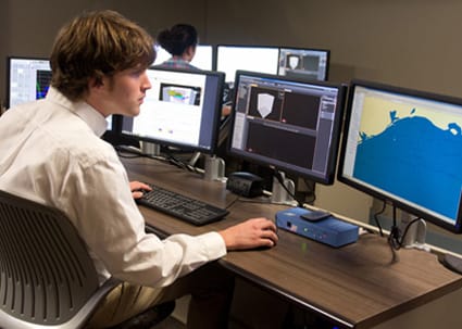 Student sits at desk monitoring multiple computer screens.