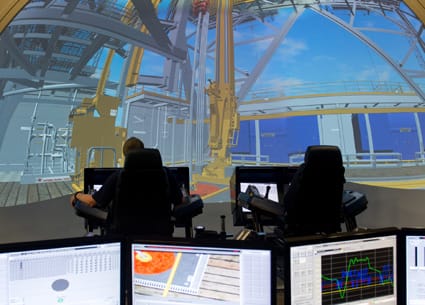 Student sits at a workstation facing a large drilling simulation.