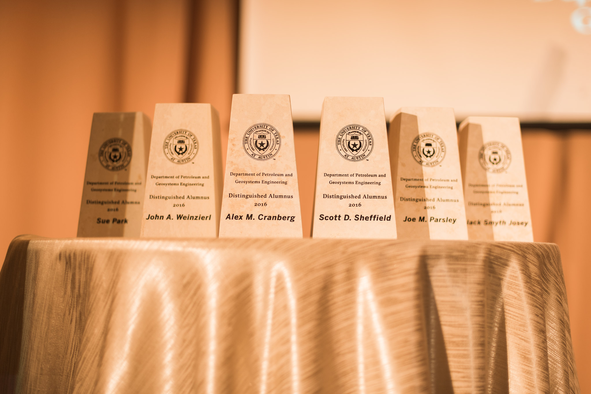 Six engraved awards sitting on table covered in white table cloth.