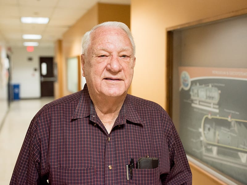 Kenneth Gray standing in long hallway in front of blackboard.
