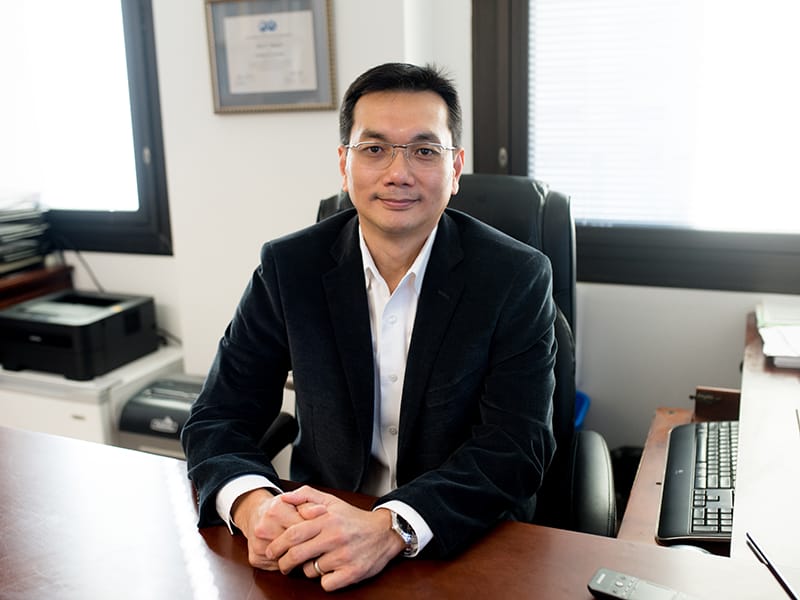 Quoc Nguyen sitting at desk with hands clasped in front of him.