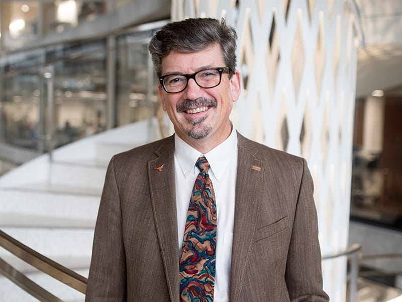 Jon Olson smiling in front of staircase in EER building on UT Austin campus.