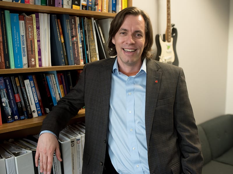 Michael Pyrcz leaning against bookshelf and smiling.