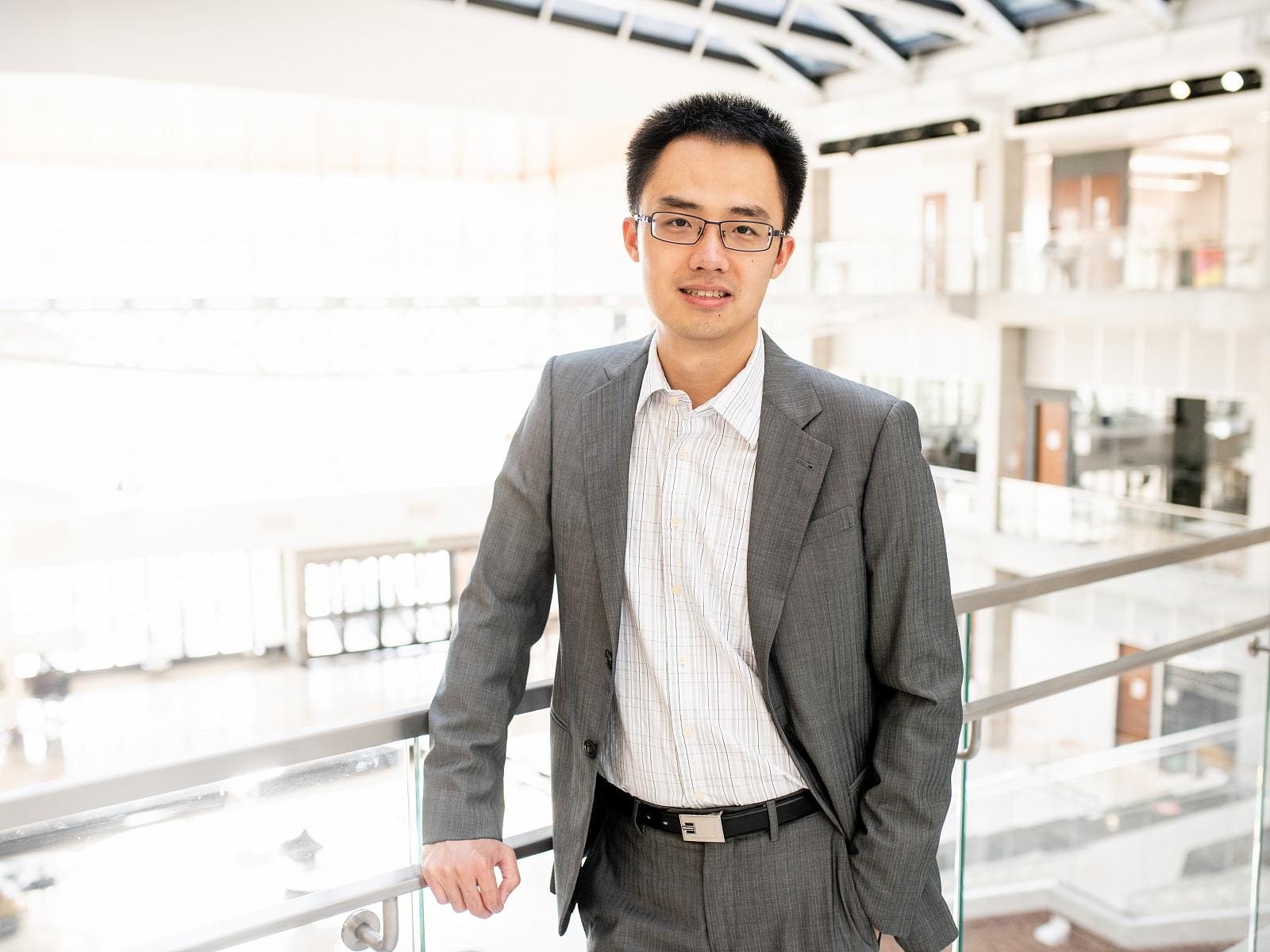 Yingda Lu smiling and leaning against railing in front of large windows.
