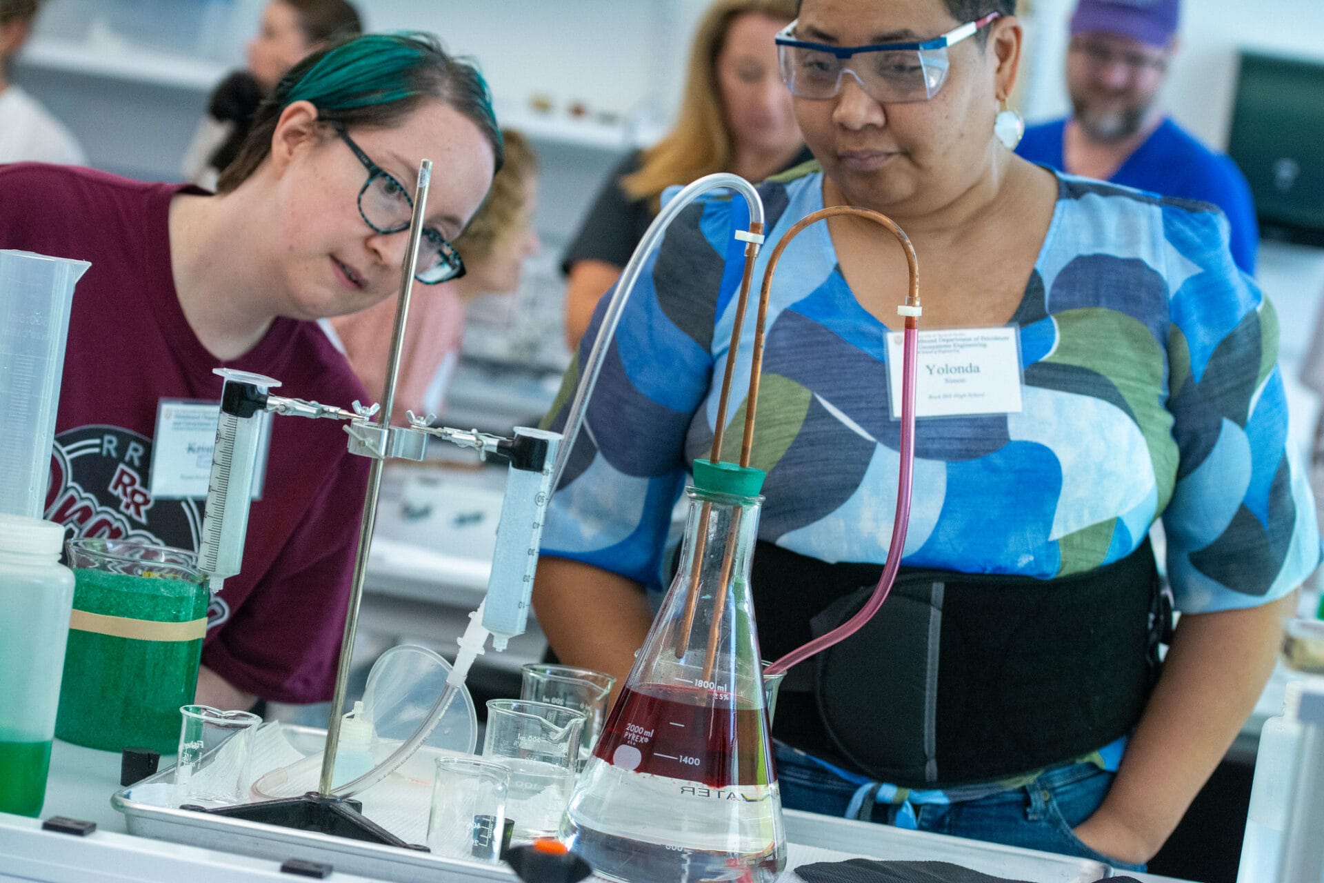 Two event participants looking at lab station with beakers, tubing, and other equipment.