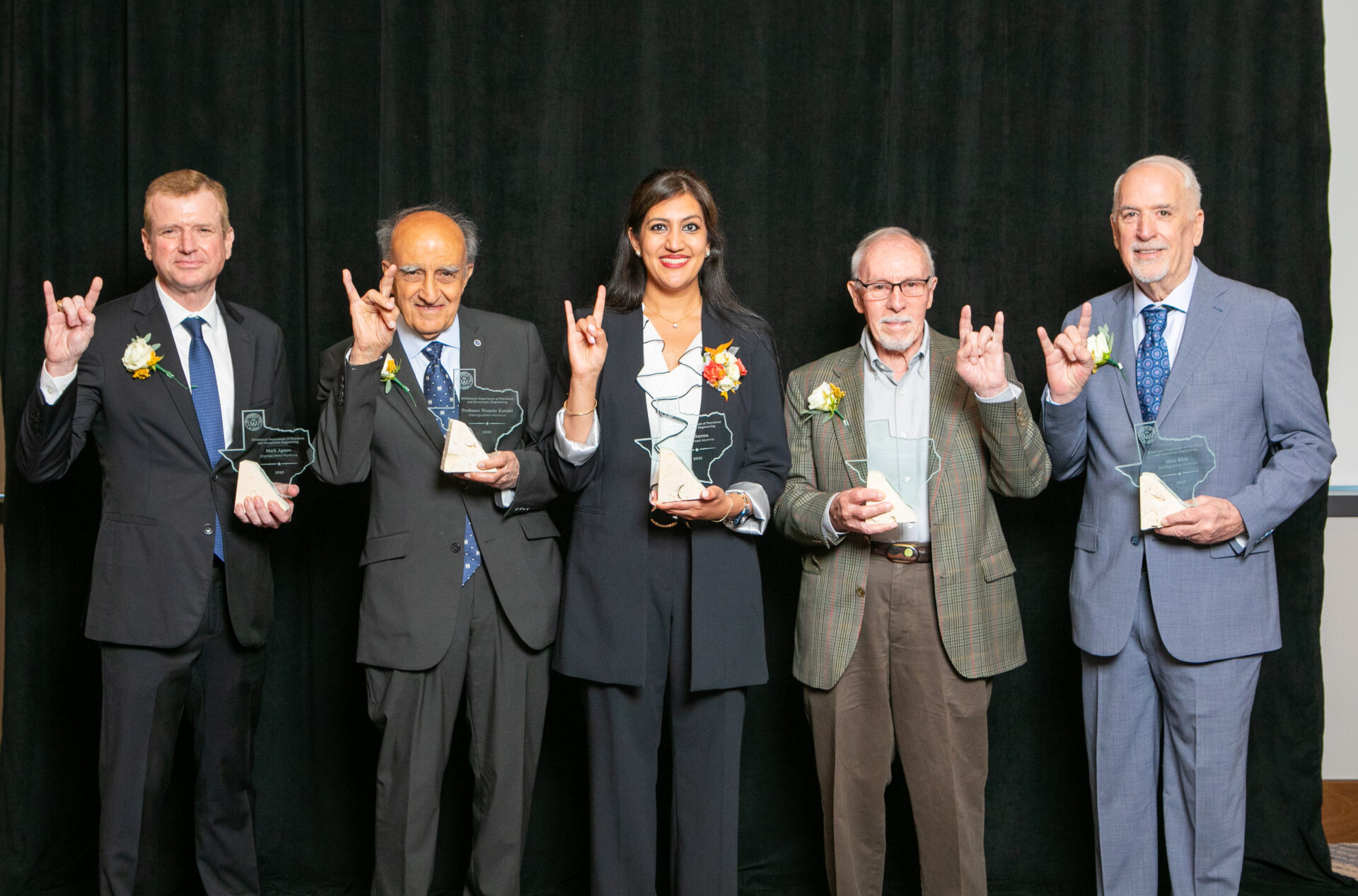 Distinguished Alumni honorees smiling while holding awards and doing hook 'em horns hand signs.