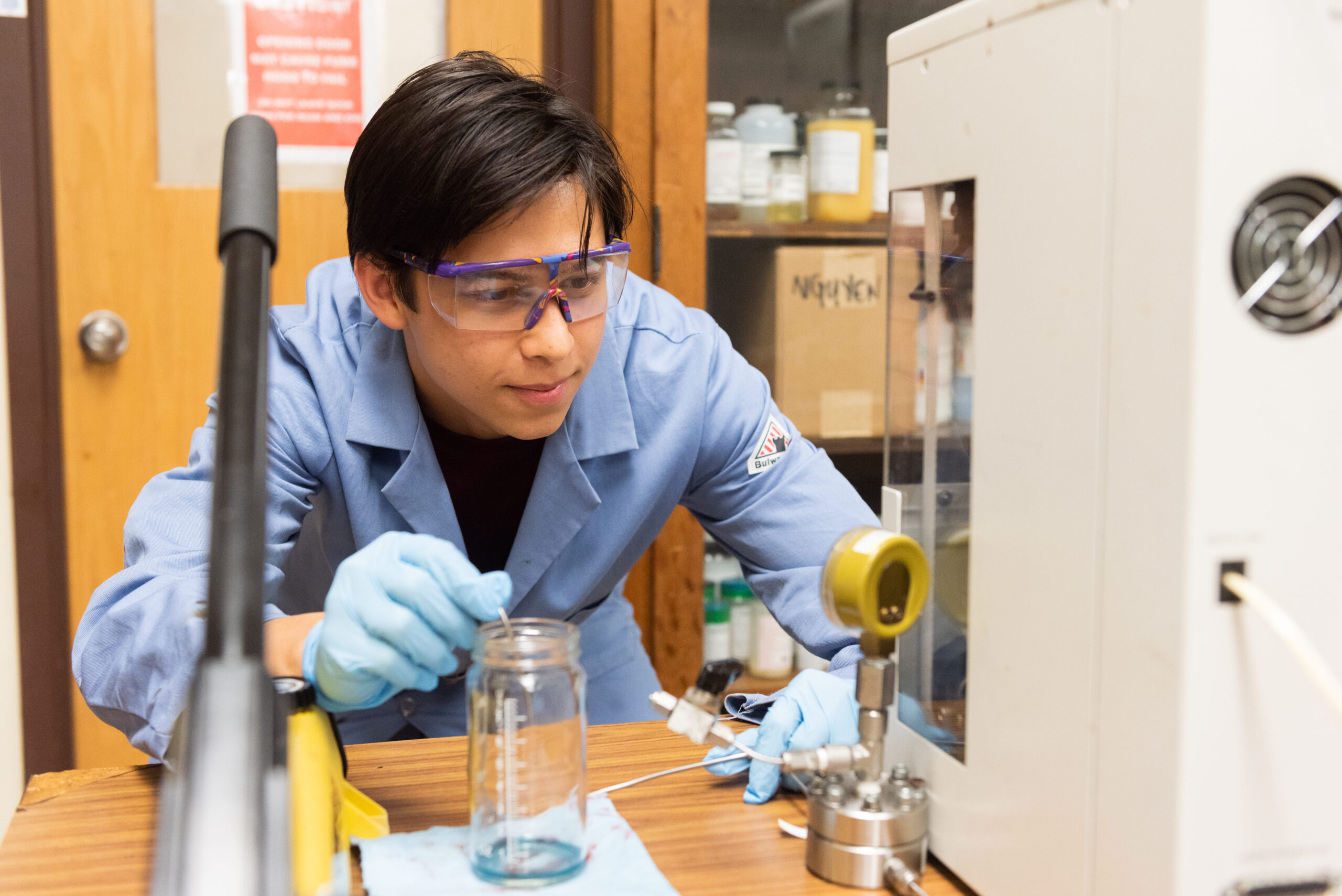 PGE student wearing lab PPE looking at various beakers and test tubes on table in lab.