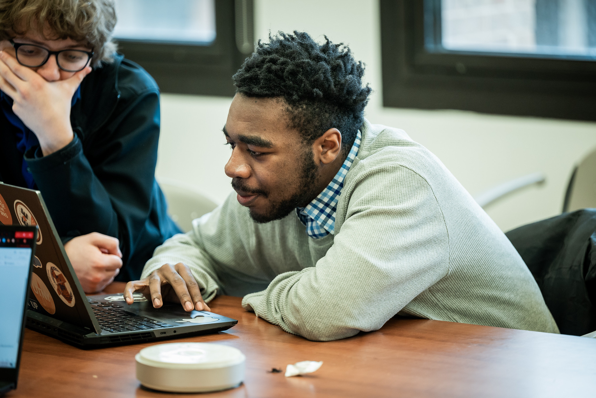 PGE student looking at laptop on table next to colleagues.