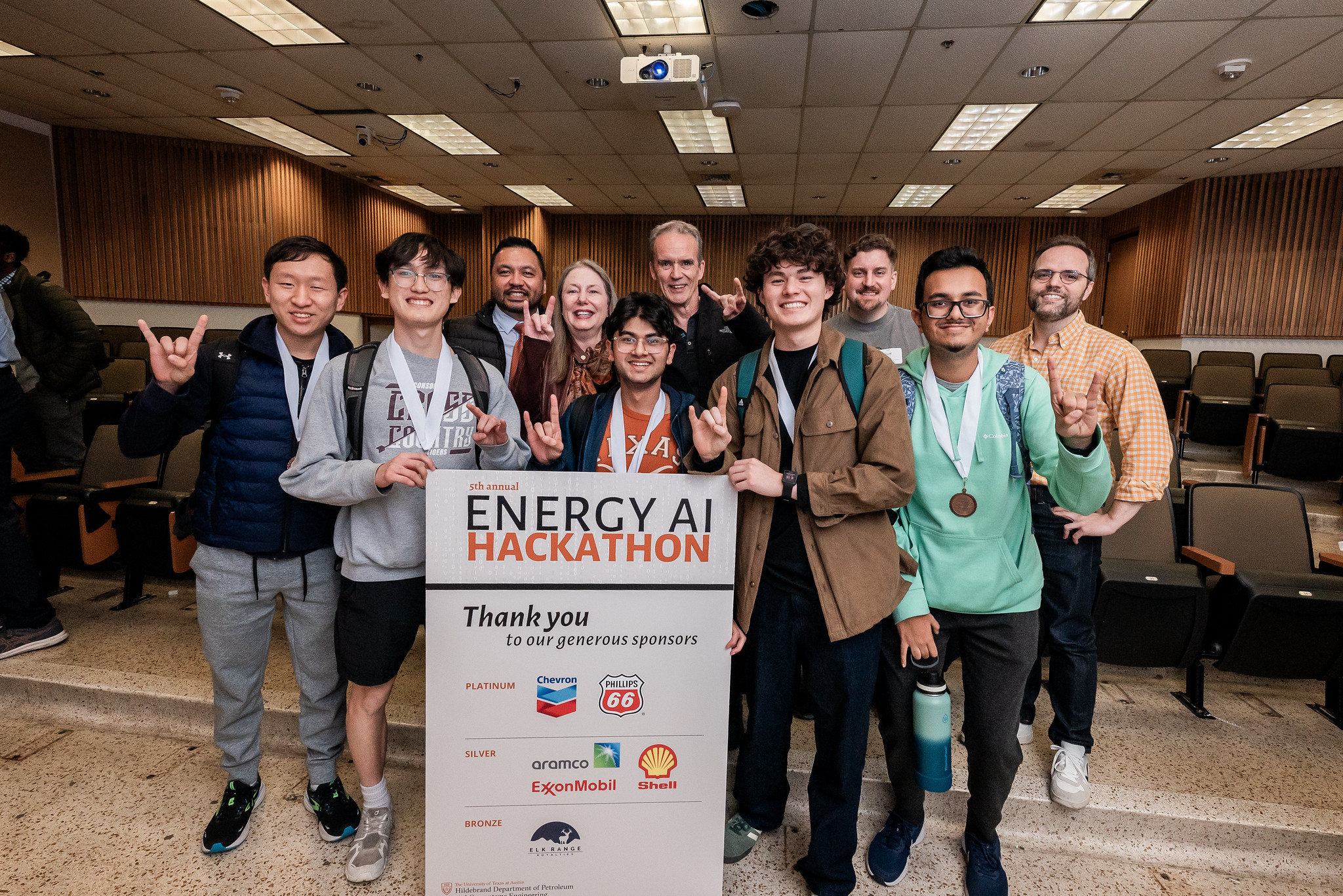 UT PGE students wearing medals and holding sign for annual Energy AI Hackathon event.