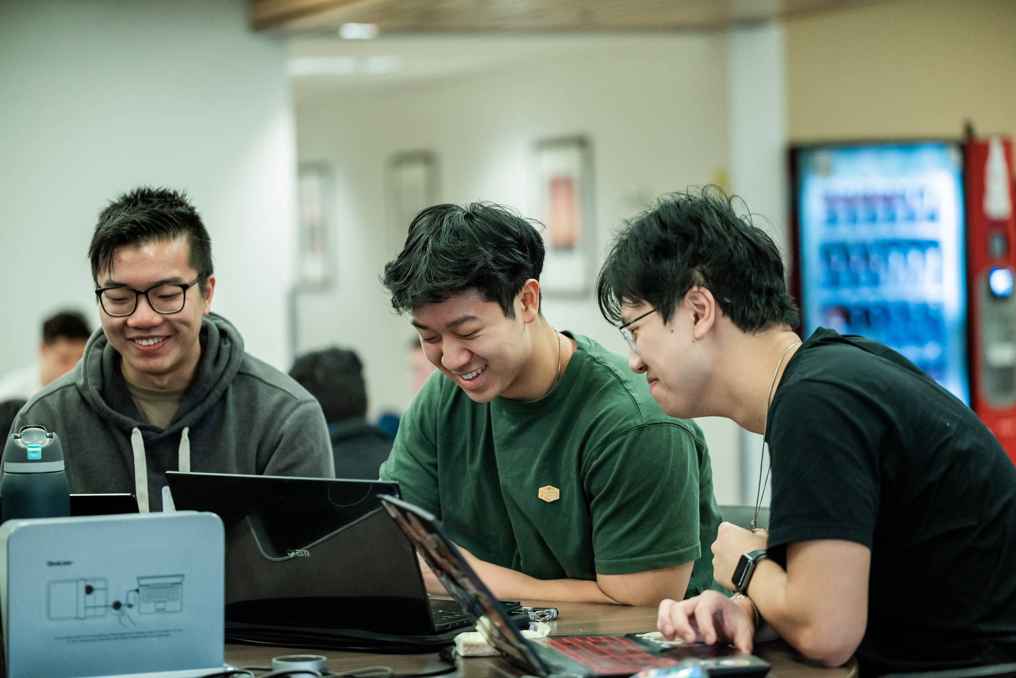 UT PGE students laughing together in front of laptops in a common study area.