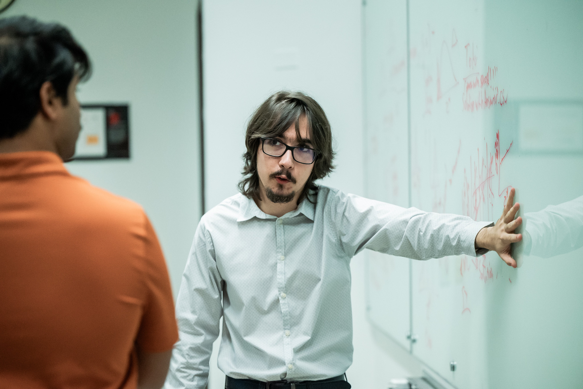 PGE student pointing to whiteboard with research notes written on it while talking to colleague.