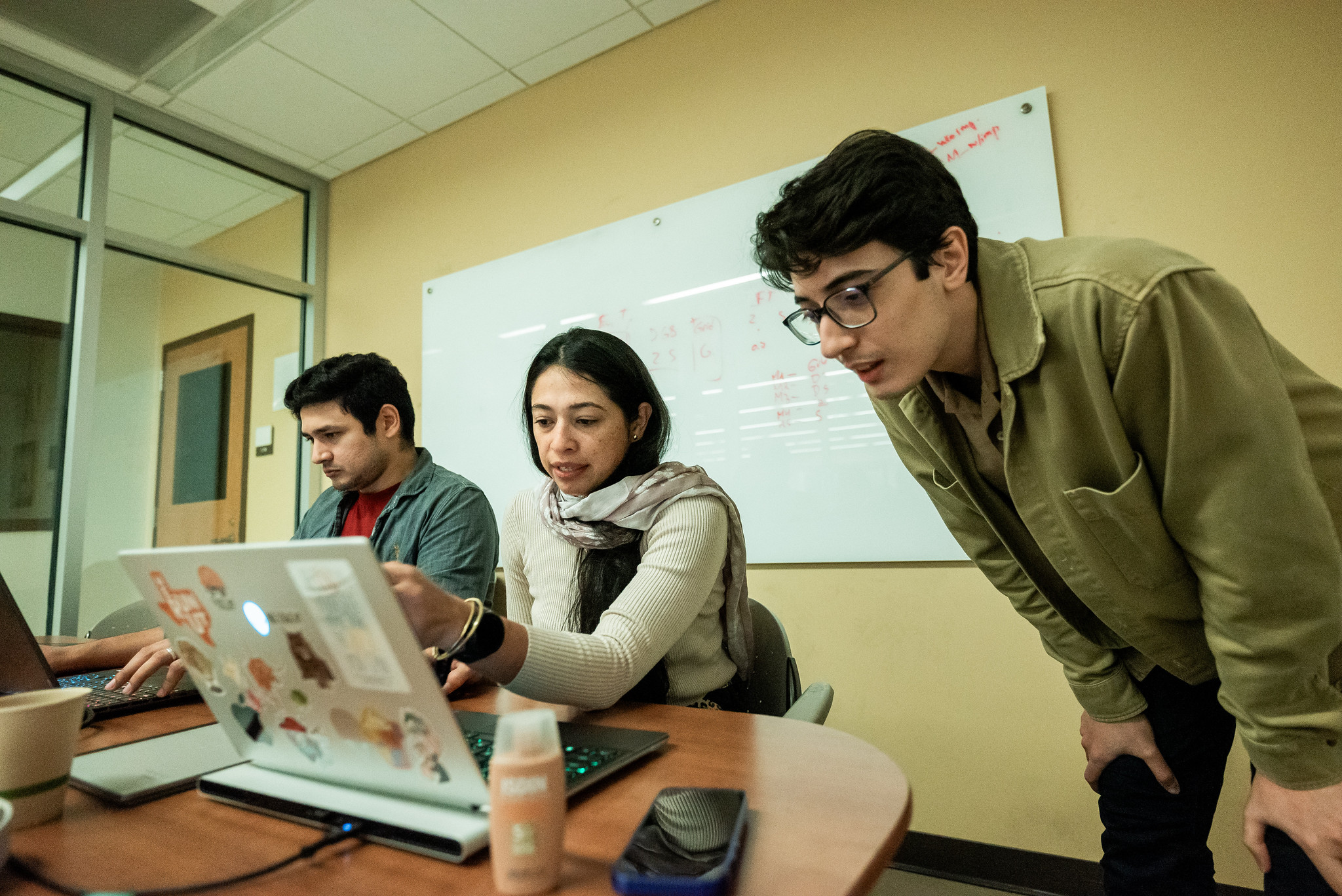 PGE students gathered around a table, looking at laptop screens and talking.