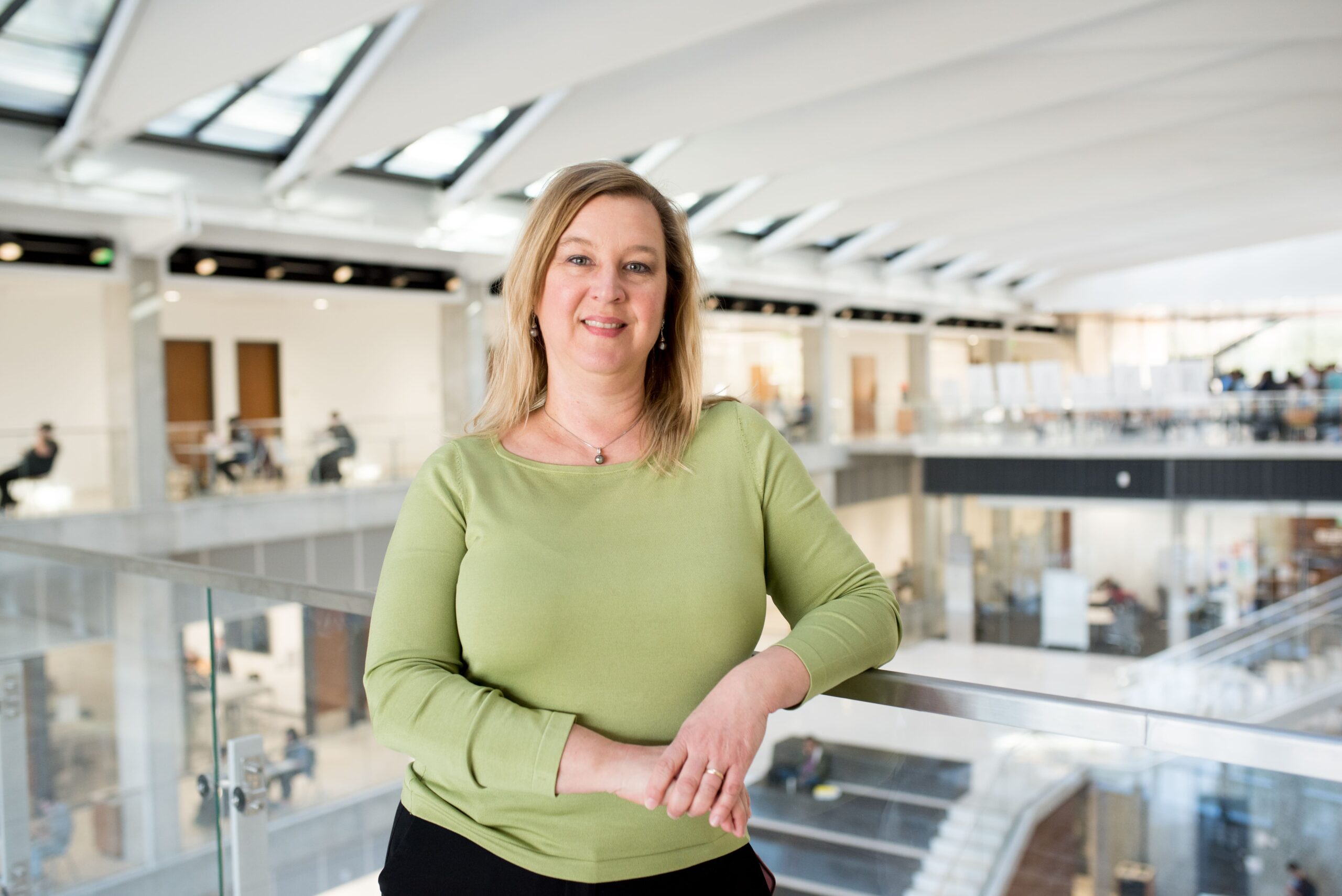 Deborah Hempel-Medina smiling and leaning against railing on upper floor of EER building on UT Austin campus.