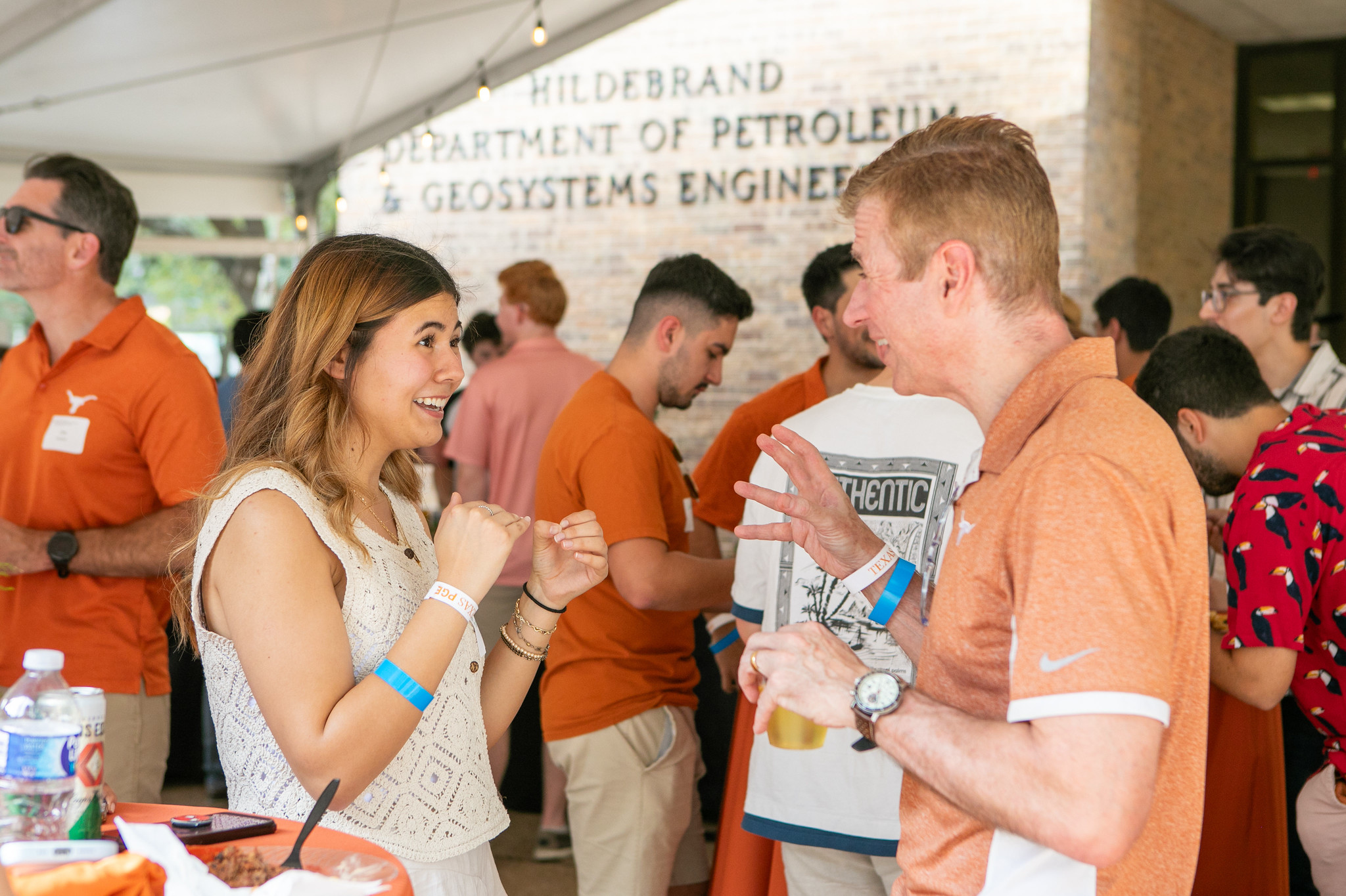 UT PGE alumni having active discussion in the middle of crowd in front of PGE building on UT Austin campus.