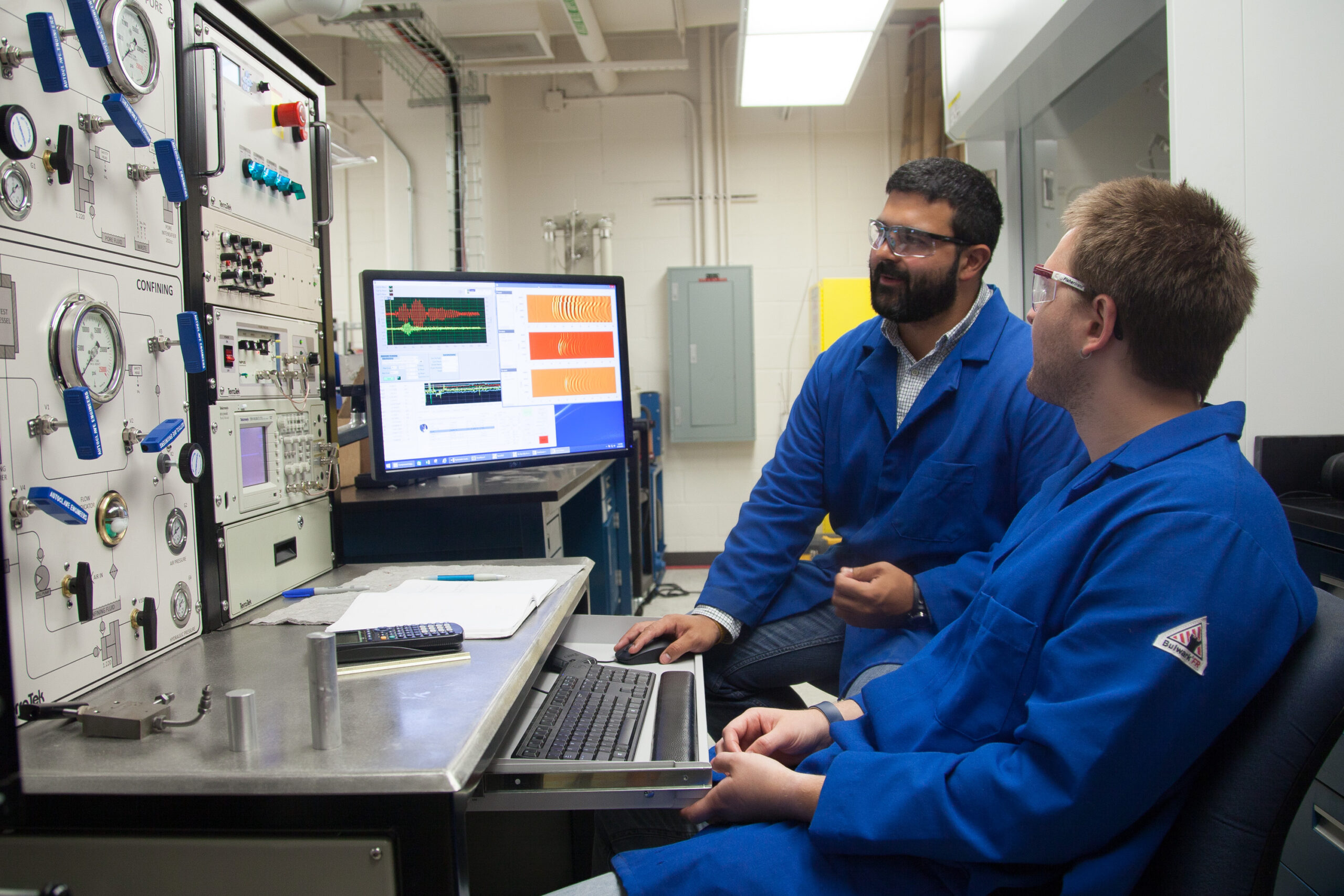 Two researchers looking at computer monitors and wall of different pressure readers.