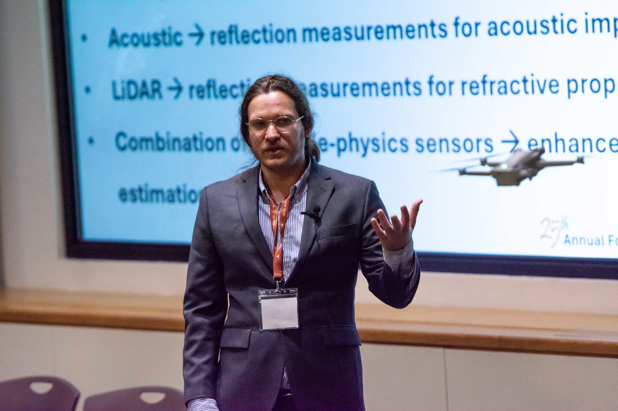 Presenter standing in front of large projector screen with small drone device flying in front of him.