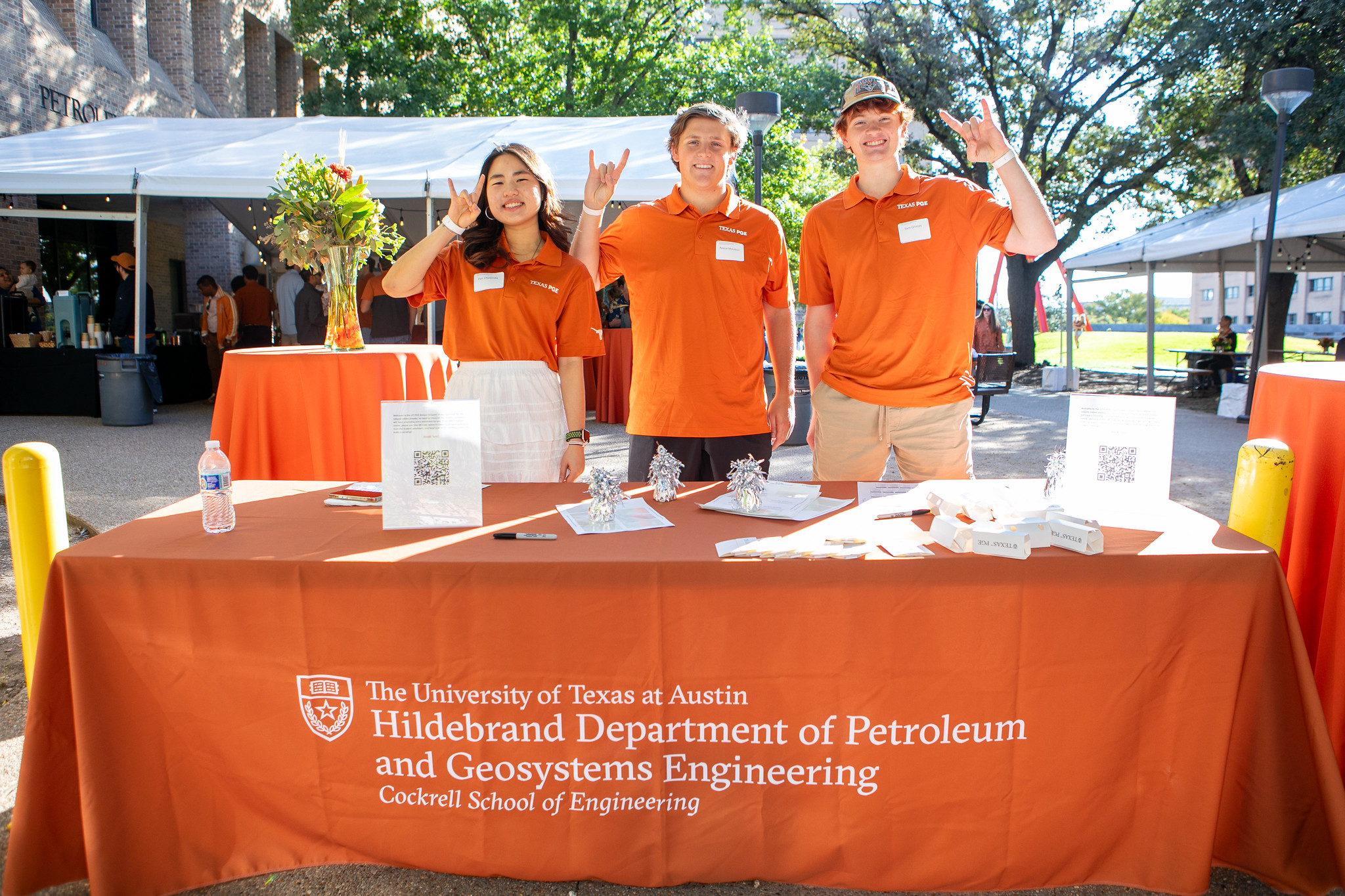 PGE student staff members doing hook 'em horns hand sign behind table outside.