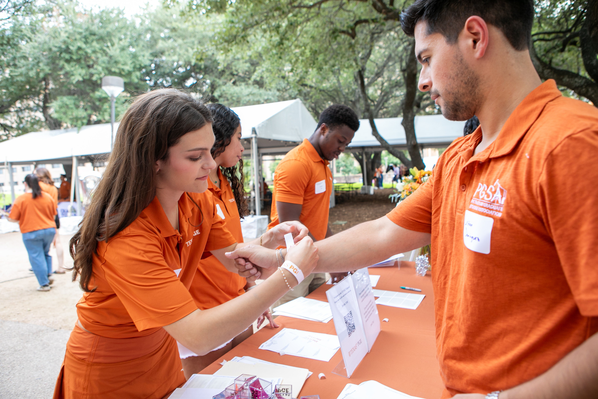 PGE staff members putting wristbands on visitors at table on UT Austin campus.