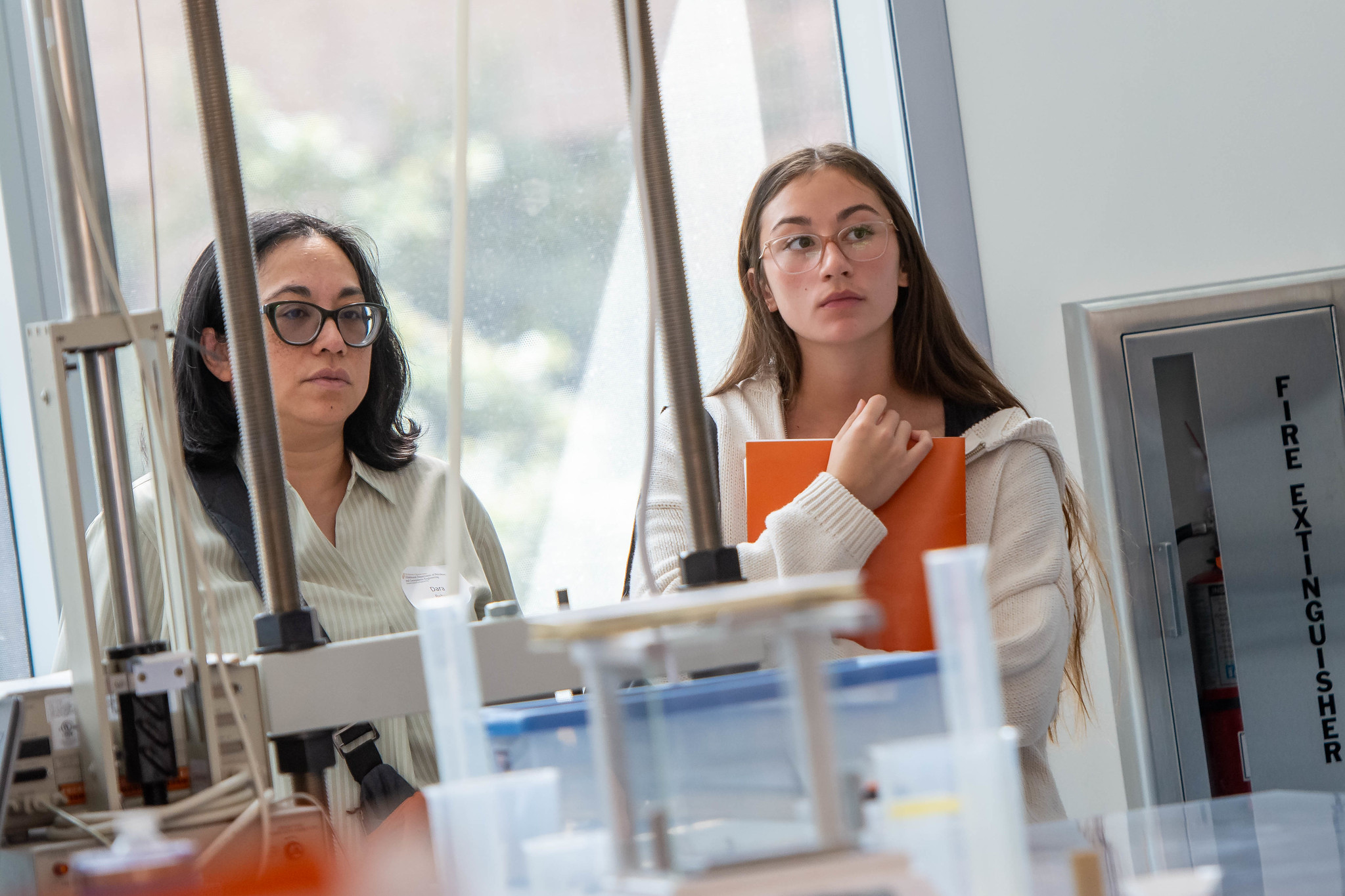 PGE students looking at presentation in lab behind table with research equipment.