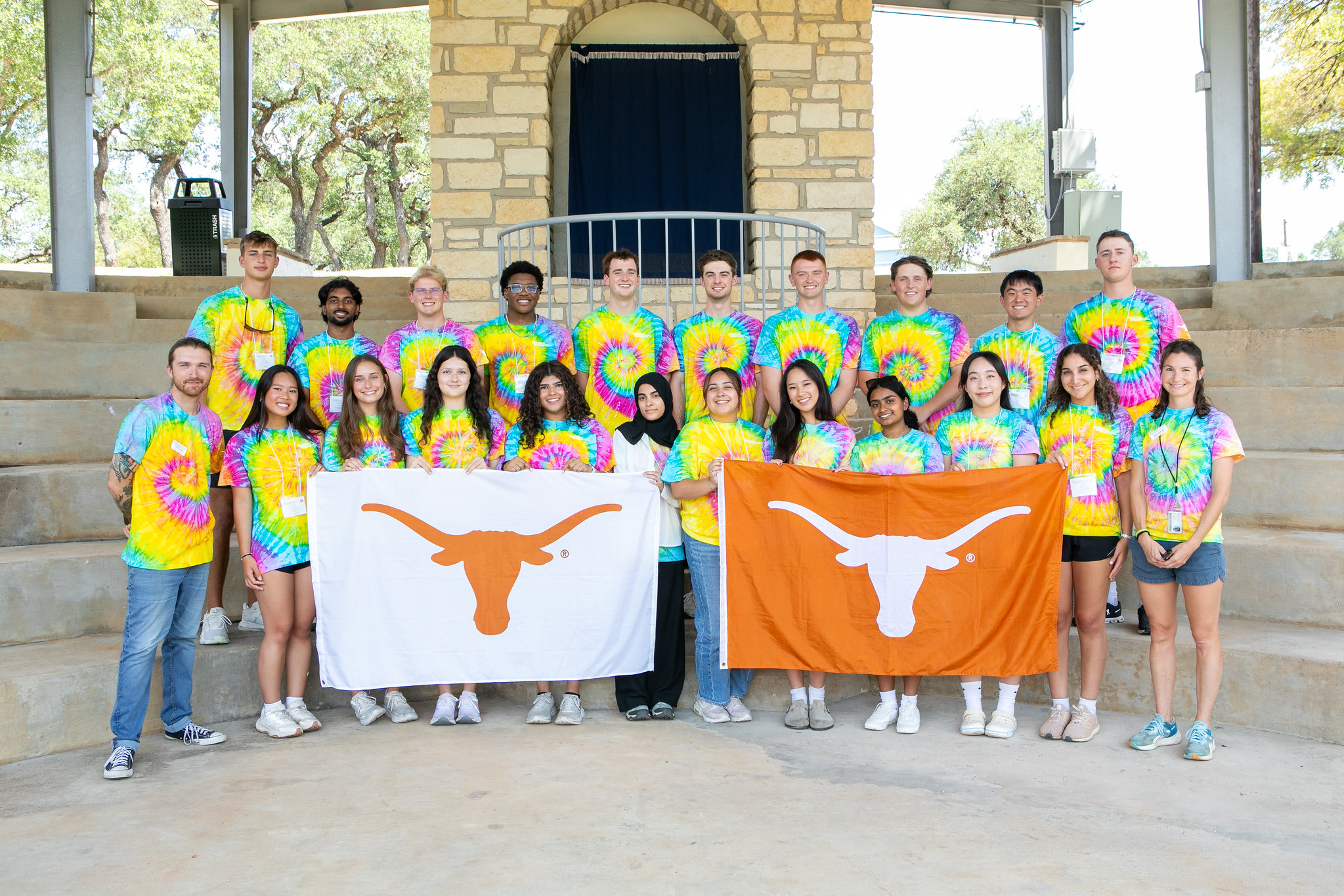 PGE students wearing UT Austin tie-dyed t-shirts smiling in group while holding UT Austin flags.