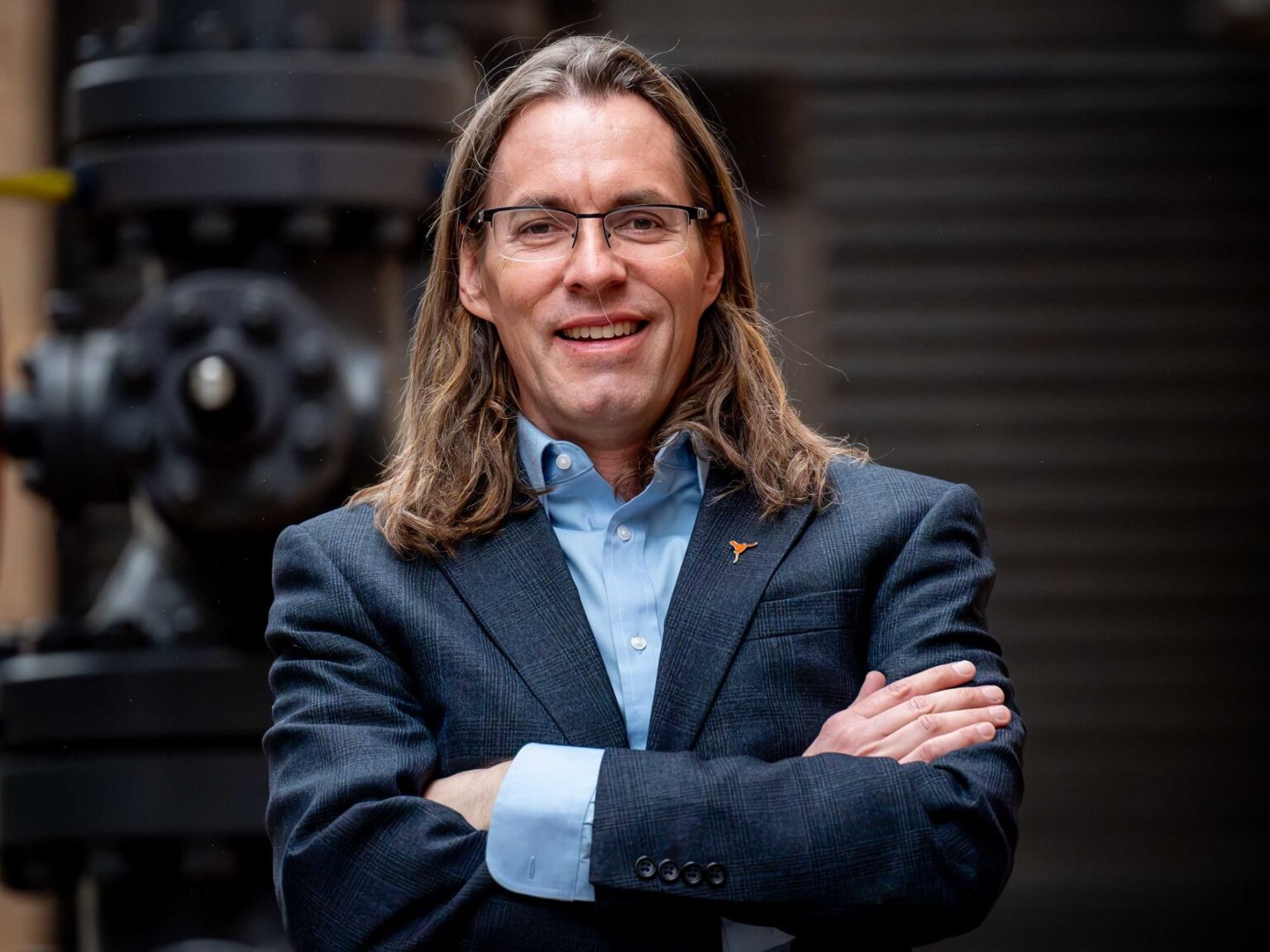 Michael Pyrcz smiling with arms crossed in front of large machine with pressure valve.