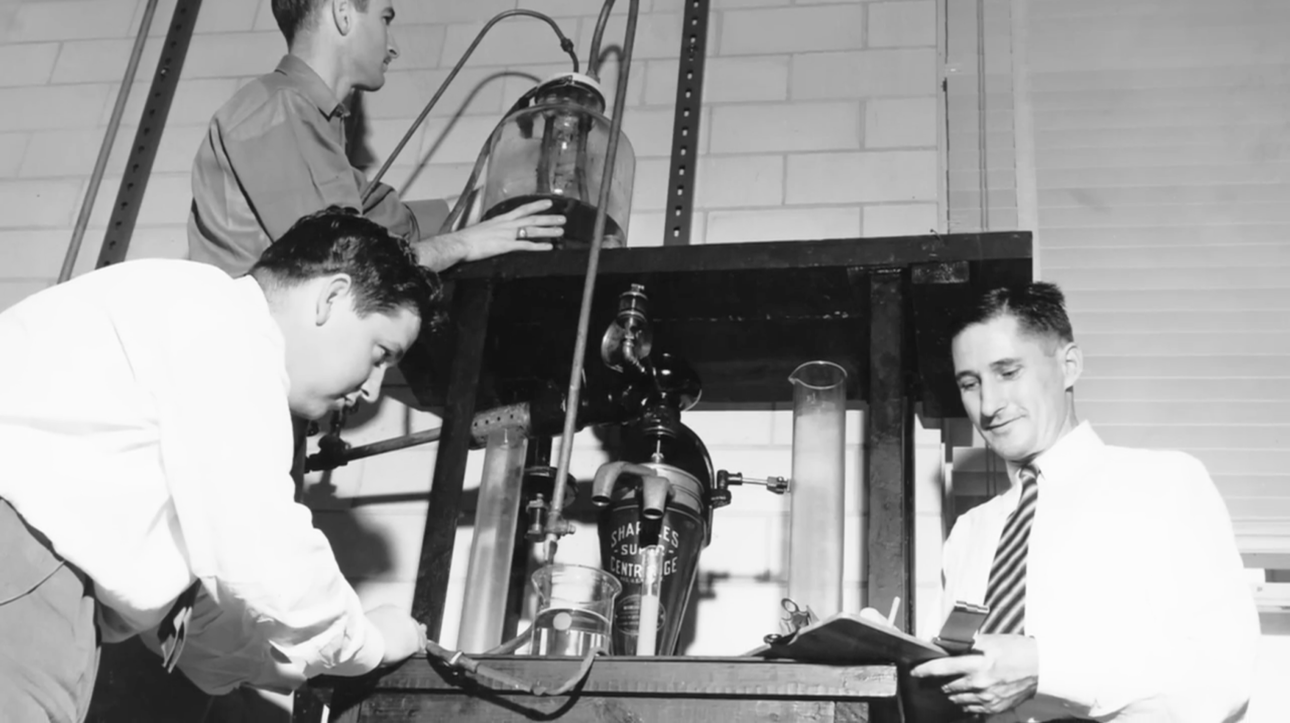 Three men at the UT Austin petroleum and geosystems engineering department work with 1950s working with a Sharples Super Centrifuge equipment