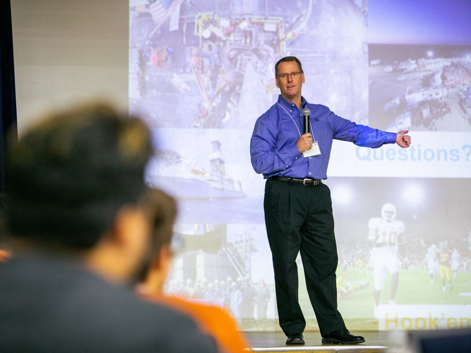 Man standing on stage in front of presentation, holding microphone.