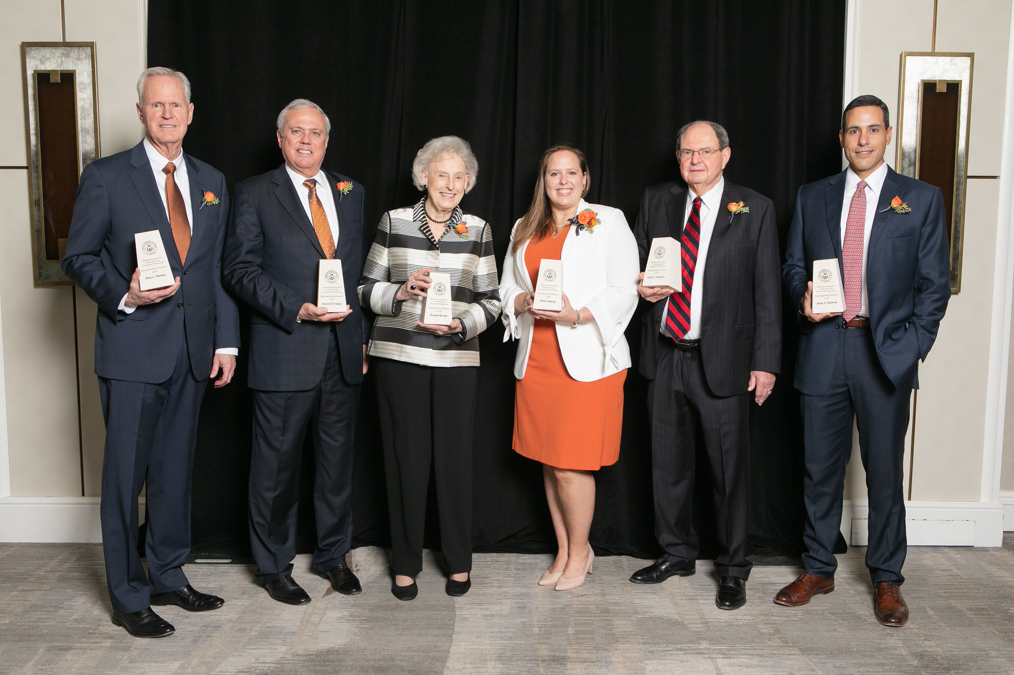 Distinguished alumni award recipients holding their awards and smiling.