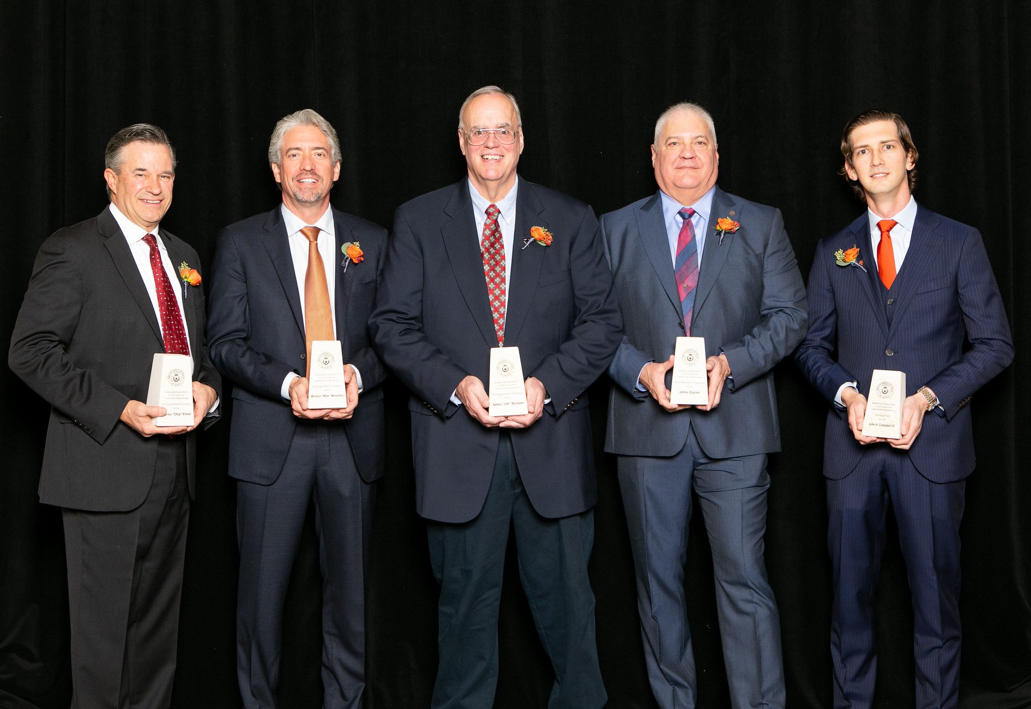 Distinguished alumni award recipients holding their awards and smiling.