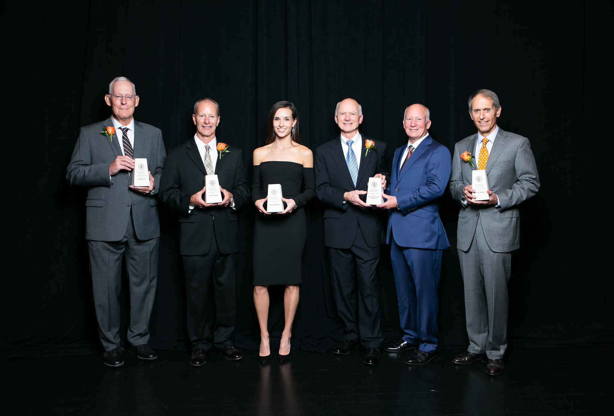 Distinguished alumni award recipients holding their awards and smiling.