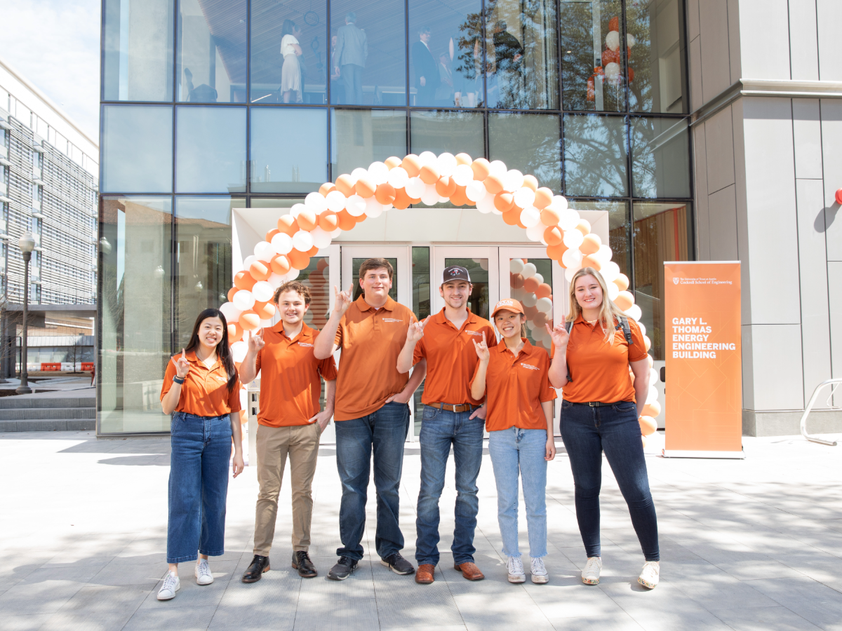 Students standing underneath balloon arch in front of the GLT Building on UT Austin campus.