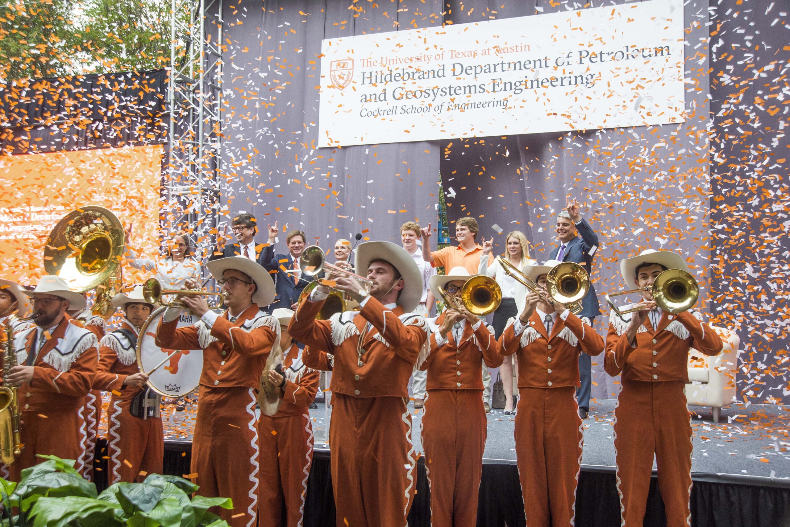 UT band playing instruments while confetti rains down in front of stage with large banner reading: "Hildebrand Department of Petroleum and Geosystems Engineering"